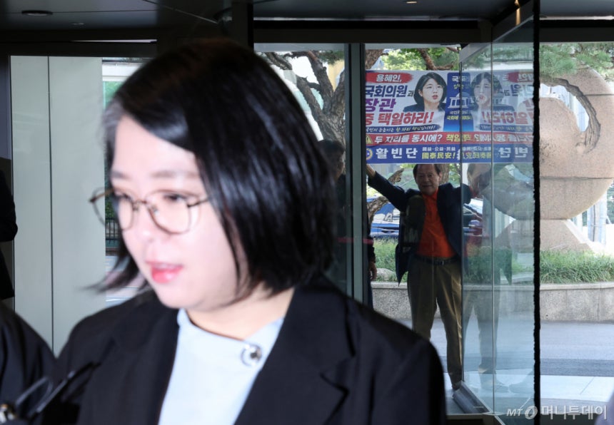 11일 오전 서울 서대문구 한국청소년활동진흥원에 마련된 인사청문회 준비 사무실로 출근하는 용혜인 성평등가족부 장관 후보자 뒤로 한 시민이 '국회의원과 장관 중 택일하라'고 적힌 현수막을 들고 있다. /사진=뉴시스
